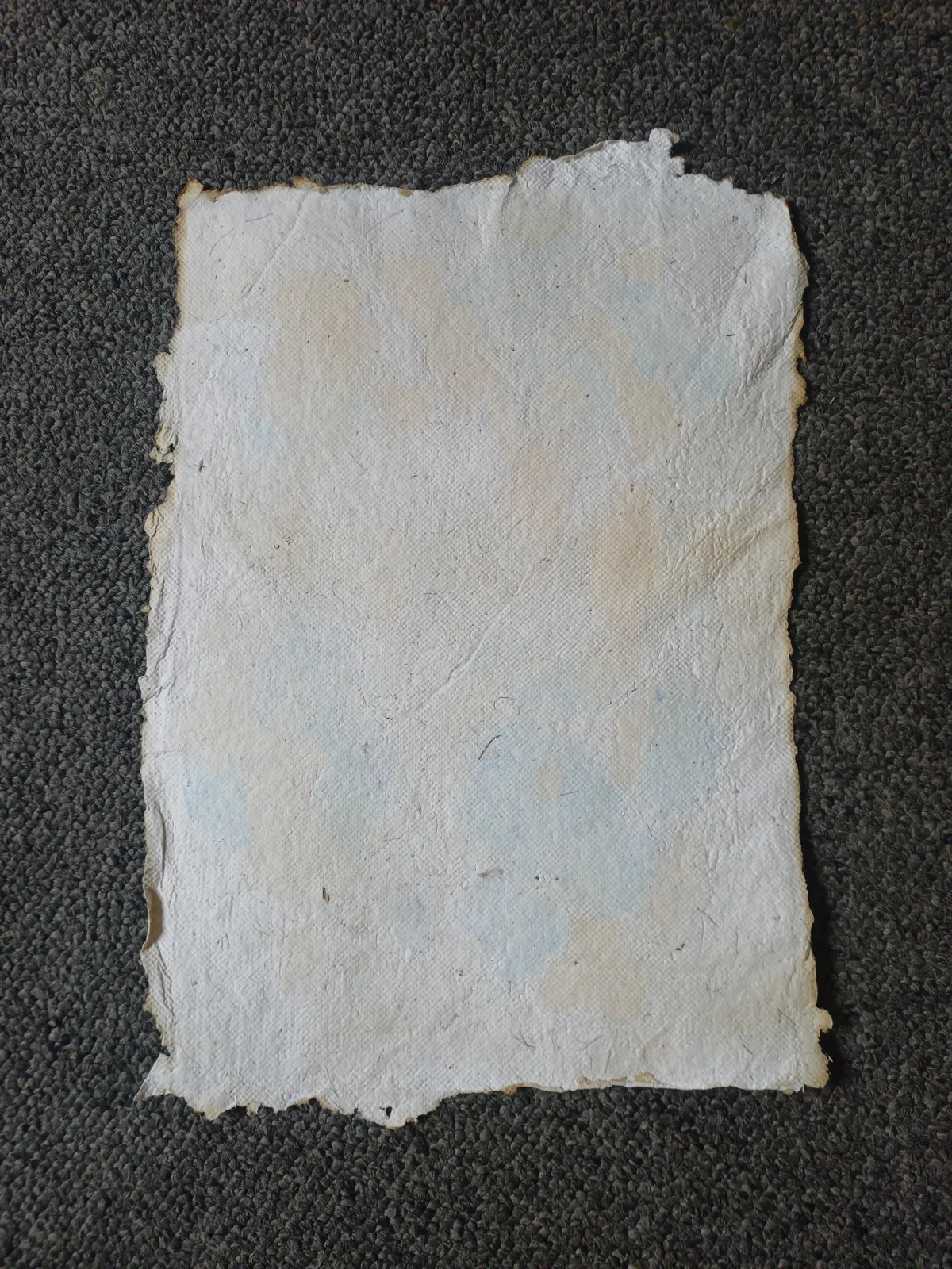 An A5 sheet of handmade paper, pale with a soft blue and cream wash and four torn deckle edges