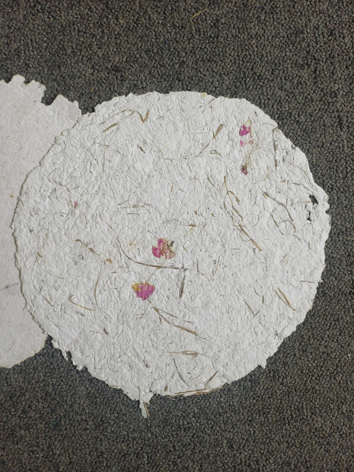 A round sheet of handmade paper 30 cm across, with pink petals and grass pressed into it
